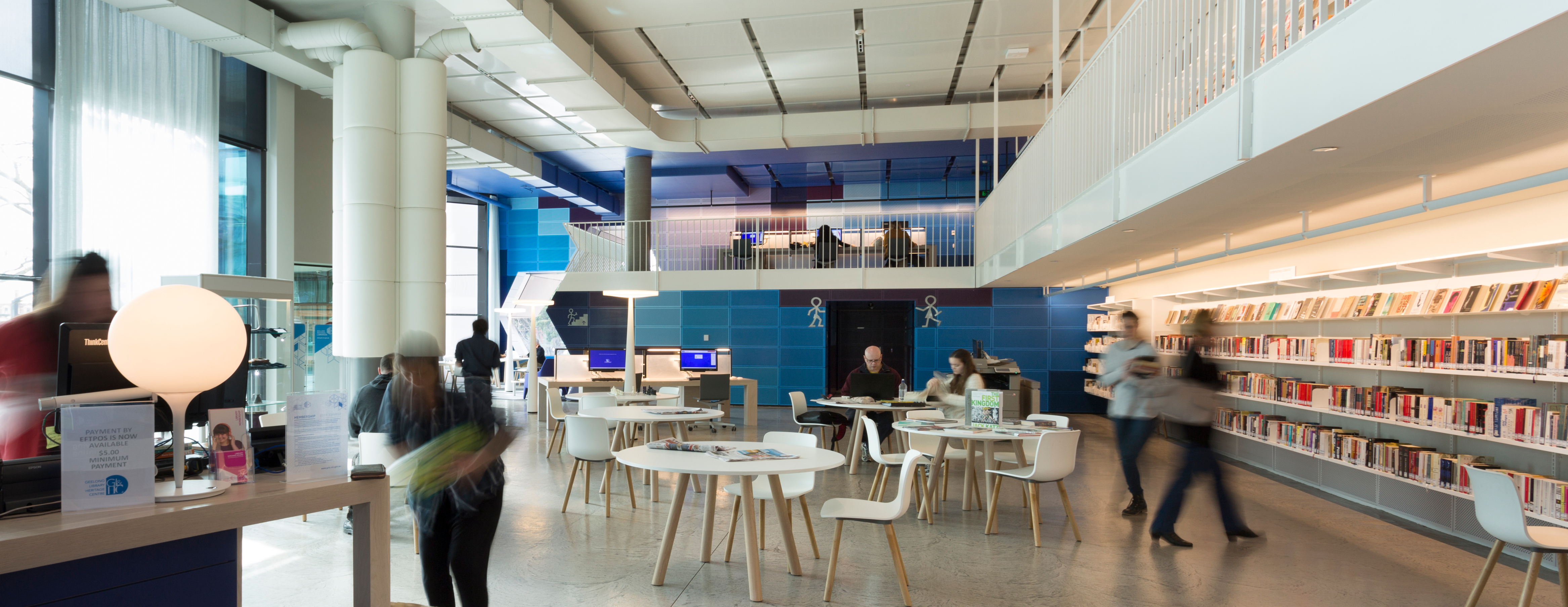 Interior image, ground floor of Geelong Library with blurred figures of people moving about space. 