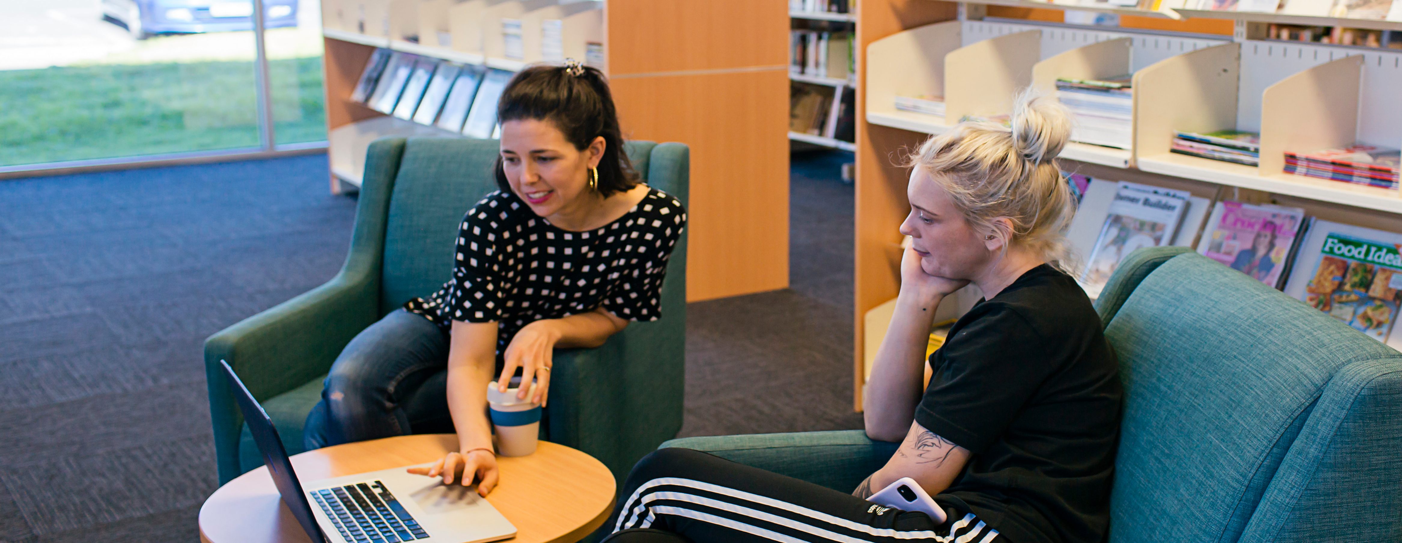 Two women look at a laptop inside a library
