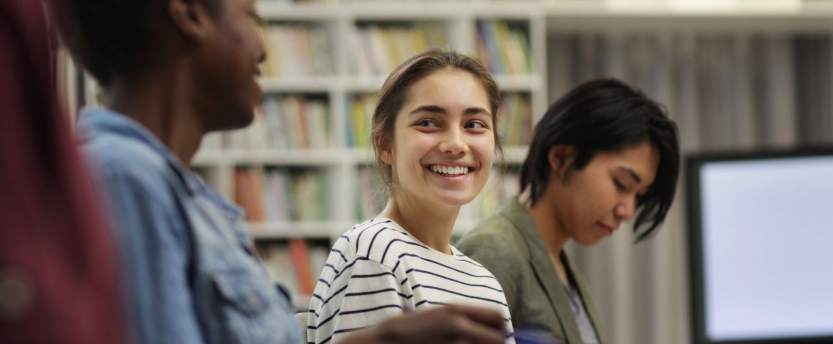 Group of three young women talking and smiling in library