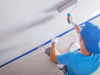 Person in blue hat and tshirt painting a white wall using a roller. View is from above.