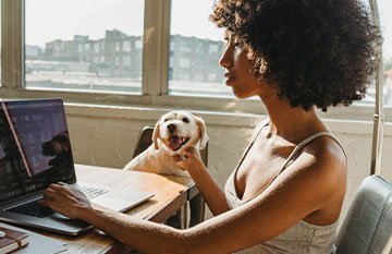 Image description: A woman sits at her computer with her dog beside her