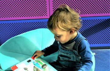 Toddler boy sitting and reading a picture book inside the Geelong Library & Heritage Centre