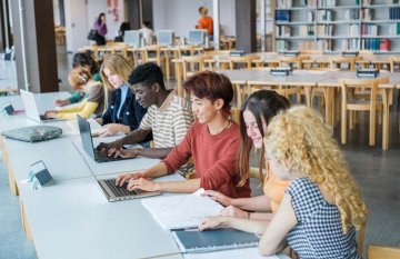 A group of diverse young adults, working together on their laptops