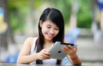 Young smiling woman sitting at outside table looking at iPad.