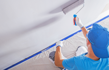 Person in blue hat and tshirt painting a white wall using a roller. View is from above.