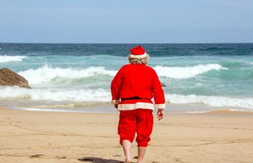 Man dressed in Santa suit walking on the beach